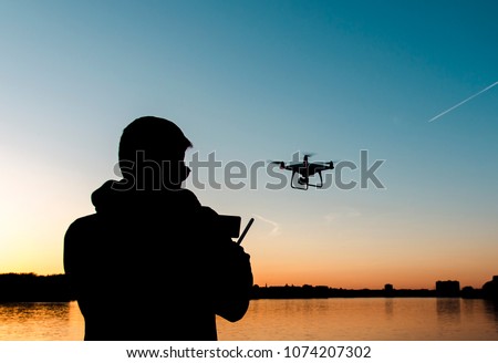 Silhouette of man flying drone by the river at sunset 