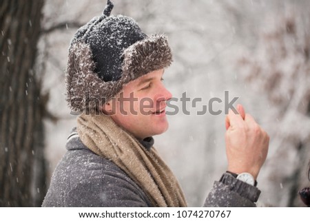 Side view of the young funny man who is showing a fig in the snow-covered park