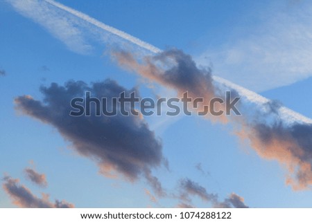 Blue sky and clouds. Plane flying through clouds leaving vapour trails.