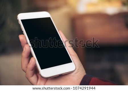 Mockup image of hand holding white mobile phone with blank black screen in cafe