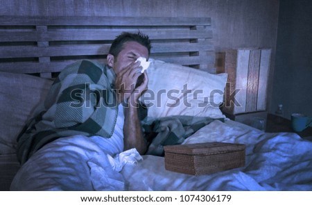 grunge edit on tired and wasted man sick at home freezing in bed covered with blanket sniffing sneezing and blowing nose suffering grippe feeling unwell in winter cold disease and temperature