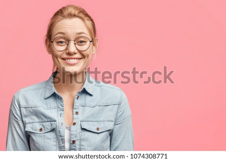 Joyful lovely young female with pleasant appearance, dressed in stylish jacket, expresses positive emotions, being satisfied with having good rest, poses against pink background. Happiness and delight