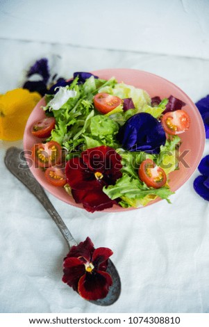 Spring vitamin salad: greens with cherry tomatoes and edible flowers (Pansy) on a light background. The concept of healthy eating.