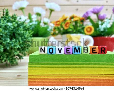 November. Colorful cube letters on sticky note block and wooden pallets as a background.