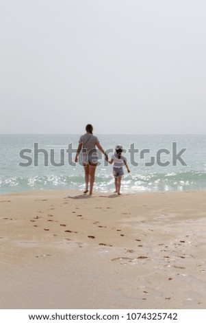 Mom and daughter are walking along the beach of the sea.