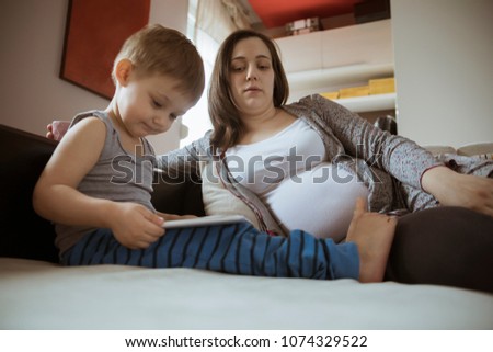 Pregnant Woman Watching Her Son Playing On The Tablet