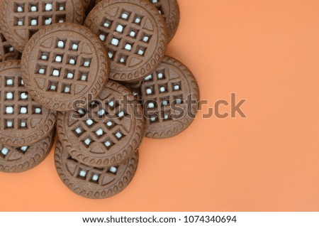 Detailed picture of dark brown round sandwich cookies with coconut filling on an orange surface. Background image of a close-up of several treats for tea