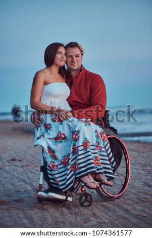 Loving couple, a woman sits on her husband's lap, resting on a beach against a background of a bright dawn.