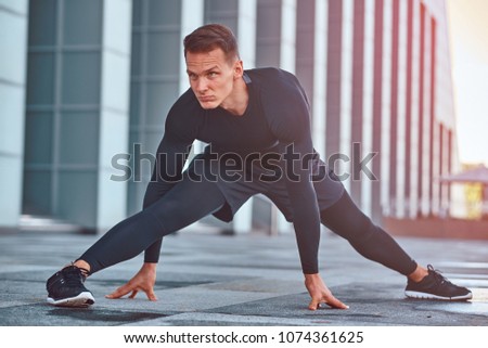 A handsome fitness man in a sportswear, doing stretching while preparing for serious exercise in the modern city against a skyscraper.