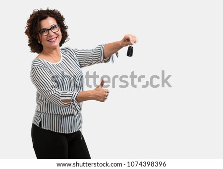 Middle aged woman happy and smiling, holding the keys of the car, confident, offering them to start your new car