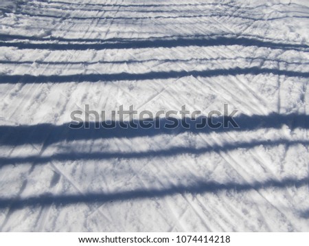 Cross country skiing path where cross country skating is used as the technique when going uphill. Shadows from trees crossing over the ski tracks.