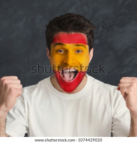 Face of young screaming man painted with flag of Spain. Football or soccer team fan, sport event, faceart and patriotism concept. Studio shot at gray background, copy space