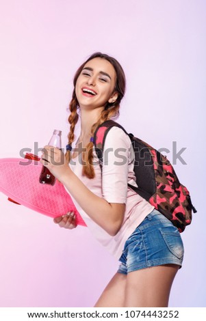 happy beautiful woman with skateboard glass bottle with soda on pink background
