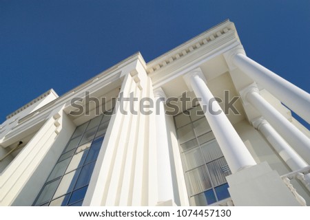 Classic style white building facade detail with pillars against clear blue sky. Modern architecture. Low angle view Royalty-Free Stock Photo #1074457130