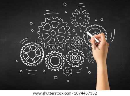 Female hand holding white chalk in front of a blackboard with gears drawn on it
