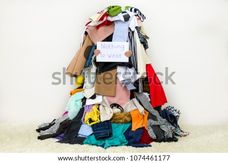 Woman covered with pile of different cloth holding Nothing to wear table sign Royalty-Free Stock Photo #1074461177