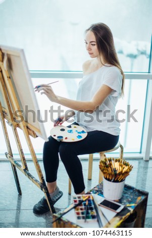 Pretty natural looking artist girl painting a picture looking at canvas in her workshop . Art, creativity, hobby, job and creative occupation concept