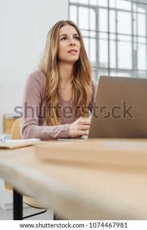 Young long-haired blonde woman sitting in front of computer at office