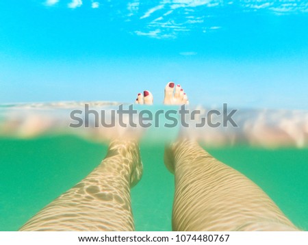 creative shot of 2 female legs relaxing under the water with pink polished nails on the water surface and blue sky in the background