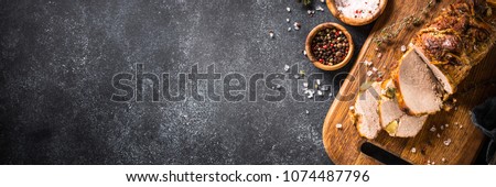 Roast pork meat with herbs and spices on black stone table. Long banner format Royalty-Free Stock Photo #1074487796