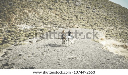 Couple riding horses around countryside in nature with their dogs following them - Happy lovers having fun on summer day - Travel, healthy lifestyle, love between people and animals concept