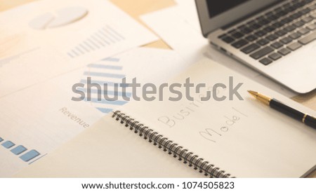 Opened notebook page with word business model on paper with blank screen laptop, pen and business documents on wooden table in office. Business plan, idea and project model concept.
