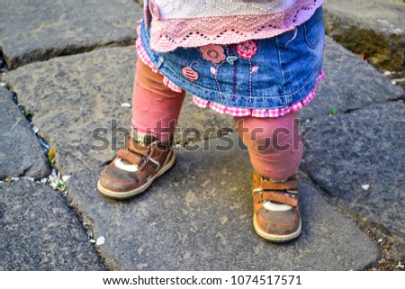 A sweet little girl walks in the open air, on a warm spring day. The baby in the shoes learns to walk on the street, the baby stands on stone tiles.