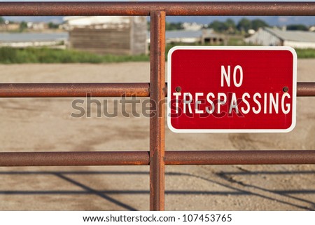 red no trespassing sign on an iron gate with out of focus farm building behind