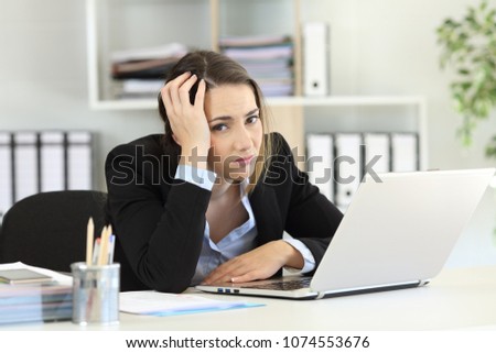 Worried office worker looking at camera sitting in a desk at workplace