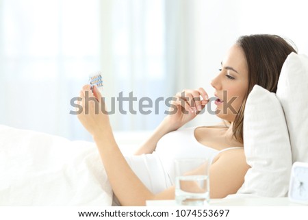 Side view portrait of a serious woman taking a contraceptive pill on the bed at home Royalty-Free Stock Photo #1074553697