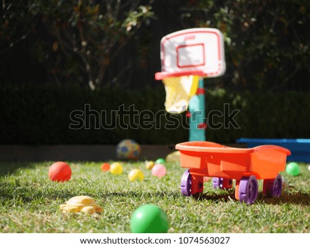 Children's outdoor play yard area with scattered toys balls, cart, basketball ring