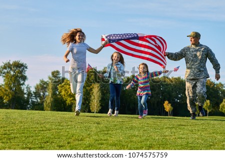 Shot of patriotic family running with flag. US soldier and his happy family.