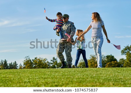 Soldier with his family are walking with usa flags. Father came back grou US army and wealking with his daughters and wife on the grass.