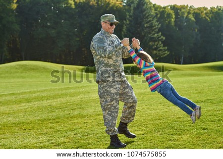 Reunion of soldier and his little daughter. Happy military man and little girl are playing together on the grass.