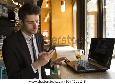 young businessman uses a phone, laptop, drinks tea in a cafe