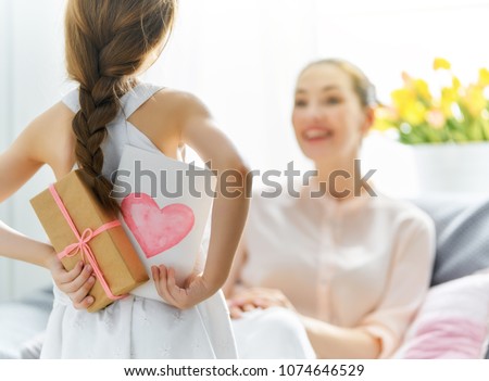 Happy women's day! Child daughter is congratulating mom and giving her postcard and gift. Mum and girl smiling and hugging. Family holiday and togetherness.