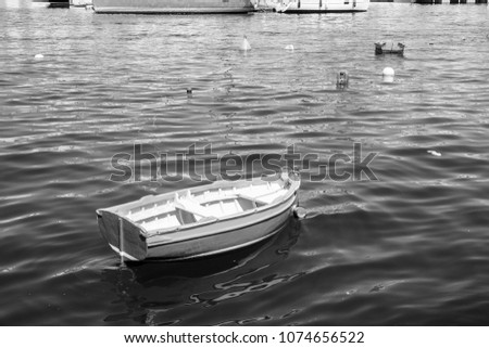 Colored buoys floating in port of Malta for mooring of yachts. A wooden cheap boat among the luxury ships. Black and white picture