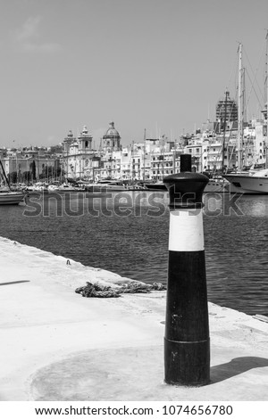 Yachts docked at the port of Malta. Boats moored in a row on the background of old city.  Mooring bollard on the harbor pier, against coastal Three Cities. Black and white picture