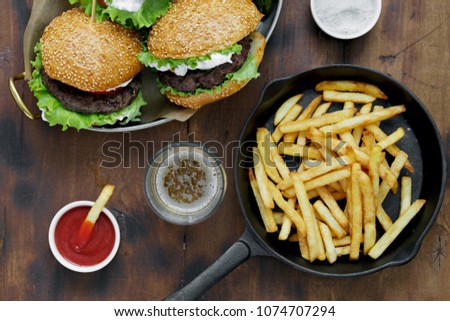 Burgers, french fries served in frying pans on wooden table with sauce, top view
