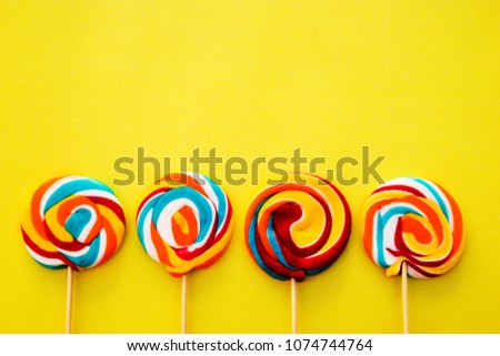 Colorful hard candy lollipop on yellow pastel background. Rainbow sweet pattern on stick flying around. Christmas holiday design concept elements.