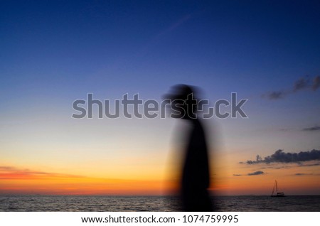 Motion blurred silhouette of man on the beach and the ship floating in the sea at sunset background. Abstract picture.
