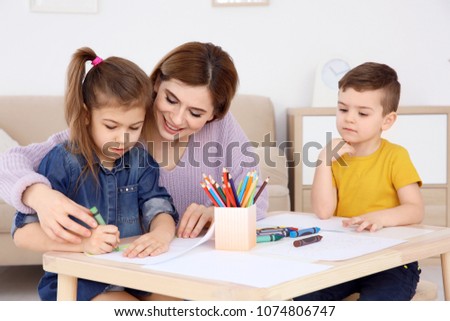 Cute little children and their nanny drawing at home