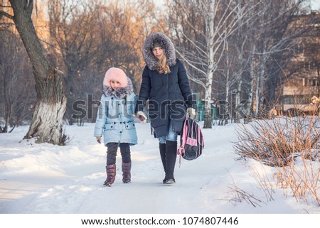 mother and daughter go from school, winter in the Park, walking family, a child with a backpack and a young mother