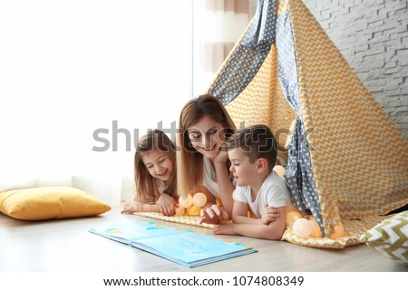 Nanny and little children reading book in tent at home Royalty-Free Stock Photo #1074808349