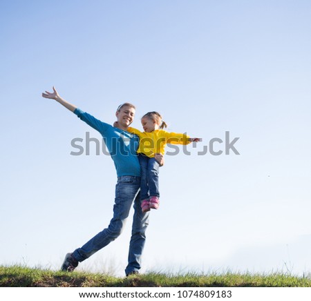 Mom and daughter are standing on the grass against the sky