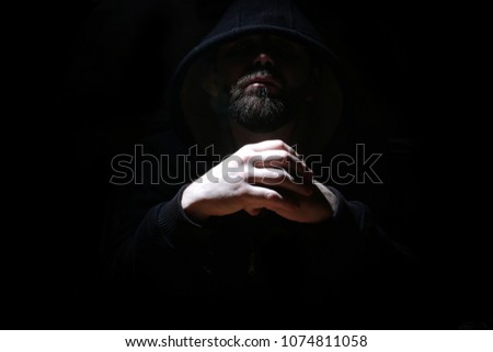 Man in a black hood and smoke on a black background
