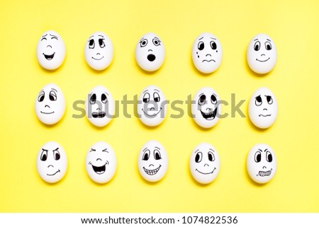 Eggs with drawn cartoon faces with various emotions in rows on yellow background