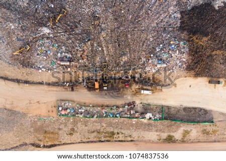 Aerial top view photo from flying drone of a modern hydraulic excavator on a field work site where an excavation works is performed in Garbage pile in trash dump or landfill.