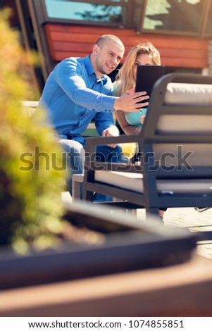 Young couple, woman and man, in street cafe drinking coffee and juice while watching pictures of holidays