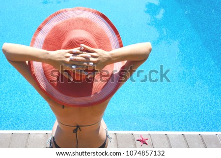 
A young slender girl in a swimsuit and hat sits by the pool and takes sunny procedures (sunbathing). Summer time 